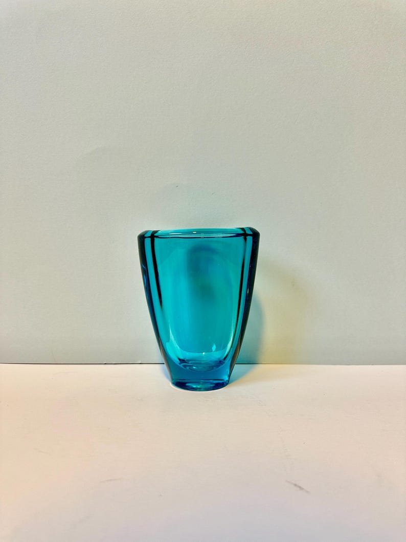 May include: A small, teal blue glass vase with a rounded, slightly flared opening and a slightly wider base.