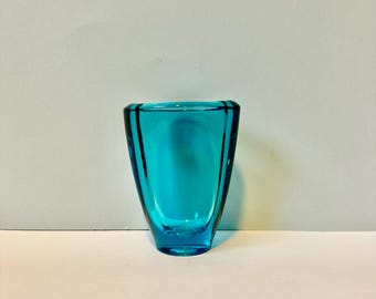 Op de afbeelding: Een kleine, turquoise blauwe glazen vaas met een afgeronde, licht uitlopende opening en een platte bodem.