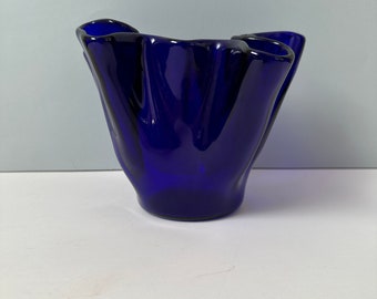 Op de afbeelding: Een diepblauwe glazen vaas met een uniek, gerimpeld ontwerp. De vaas heeft een brede opening en een getextureerde, gevouwen uitstraling, waardoor een sculpturale en elegante esthetiek ontstaat. De kleur is een rijk, verzadigd blauw.