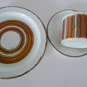 May include: A set of brown and white ceramic dishes with a concentric circle pattern. The set includes a large plate, a smaller plate, and a cup.