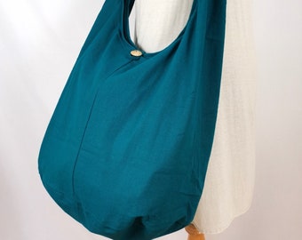 May include: Teal-colored shoulder bag with a single wooden button closure. The bag is made of a soft fabric and has a long strap. The bag is displayed on a mannequin wearing a white tank top.
