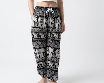 May include: Black and white loose-fitting pants featuring a repeating elephant and paisley pattern. The pants have an elastic waistband with a white drawstring cord and a relaxed silhouette that tapers slightly toward the ankles.