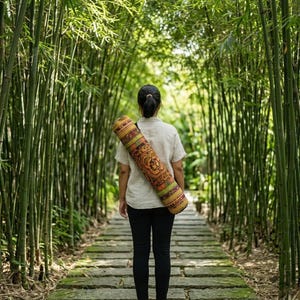 May include: A cylindrical yoga mat bag featuring a vibrant, multi-colored pattern with intricate orange, yellow, and green geometric and floral motifs, worn over the shoulder with a black strap, paired with a light beige short-sleeved shirt and black pants.