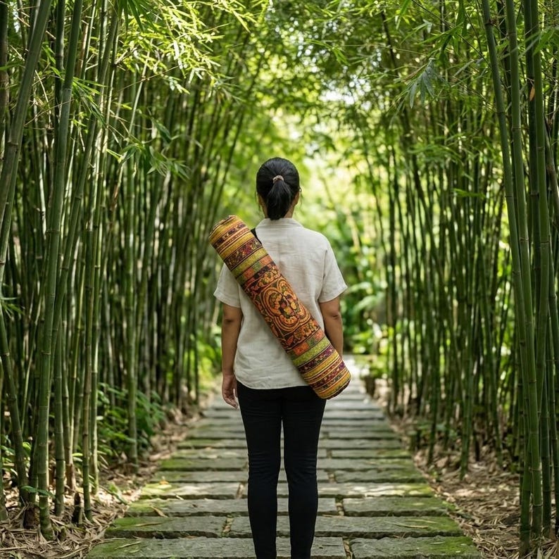 May include: A cylindrical yoga mat bag featuring a vibrant, multi-colored pattern with intricate orange, yellow, and green geometric and floral motifs, worn over the shoulder with a black strap, paired with a light beige short-sleeved shirt and black pants.