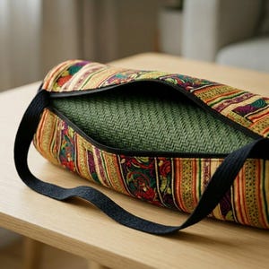May include: A cylindrical yoga mat bag featuring a vibrant, multi-colored woven pattern with stripes of red, green, yellow, and purple. The bag has a black zipper closure and black fabric shoulder straps, containing a textured olive green yoga mat.