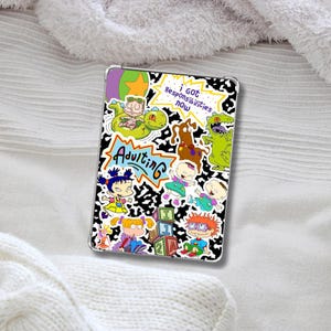 Puede incluir: Funda transparente para tableta con personajes de dibujos animados y la palabra "Adulting" en un diseño azul y blanco. La funda tiene un fondo con estampado en blanco y negro con varios personajes de dibujos animados.