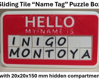 May include: A sliding tile puzzle box with a red and white design. The top reads "HELLO MY NAME IS" and displays the name "INIGO MONTOYA" on sliding tiles. The box has a hidden compartment.