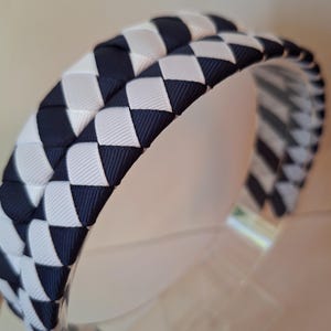 May include: A black and white braided headband with a checkered pattern. The headband is made of a soft, woven fabric.