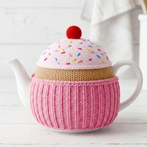 Può includere: Una teiera in ceramica bianca coperta da un rivestimento in maglia a forma di cupcake. Il rivestimento presenta una base rosa a coste, una sezione centrale color cuoio e una parte superiore rosa chiaro con zuccherini ricamati e un pompon rosso.