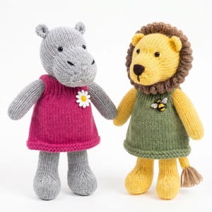May include: Two knitted stuffed animals, a gray hippopotamus and a yellow lion. The hippo wears a magenta dress with a white daisy appliqué. The lion has a brown mane and wears a green dress with a small bee appliqué on the chest area.
