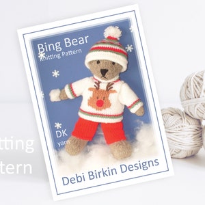Può includere: Schema di lavoro a maglia per un orso Bing che indossa un cappello rosso e bianco, un maglione bianco con un disegno di renna, pantaloni rossi e guanti bianchi. Il modello è di Debi Birkin Designs.