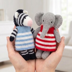 May include: Two small, hand-knitted stuffed animals. One is a black and white striped zebra wearing a light blue and white striped dress. The other is a gray elephant wearing a red and white striped dress. Both have black bead eyes.