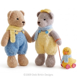May include: Two knitted teddy bears and a pull-along duck toy. The left bear is tan with a yellow scarf and blue overalls. The right bear is gray with a yellow cap, blue scarf, and yellow overalls. The yellow duck has a blue scarf and pink wheels.
