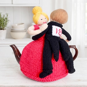 May include: A knitted tea cozy featuring a pair of figures in a dance pose. The figure on the left has yellow hair in a bun and wears a red dress. The figure on the right has brown hair and wears a black suit with a white patch displaying the number 18.