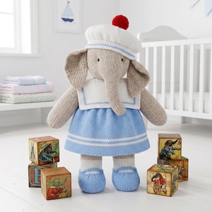 May include: A knitted elephant plush toy wearing a white sailor-style hat with a red pom-pom, a white sailor collar with blue trim, a light blue dress with white stripes, and matching light blue shoes, surrounded by four wooden alphabet blocks.