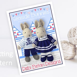 May include: A knitting pattern titled "Seaside Bunnies" featuring two knitted bunny dolls. One bunny wears a blue and white striped sweater with a skull and crossbones, the other a blue sailor dress. Yarn balls are in the background.