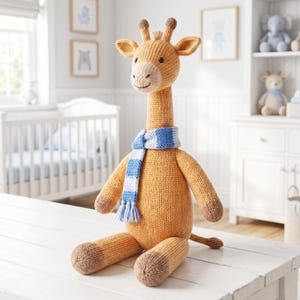 May include: A knitted giraffe soft toy with a golden yellow body, brown hooves, and two small horns on its head. The giraffe has a light cream-coloured muzzle and is wearing a blue and white striped scarf with fringe at the ends.