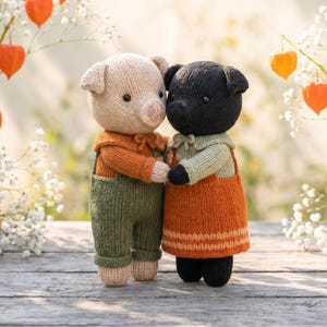 May include: Two knitted pig dolls standing side by side and holding hands. The left pig is beige with an orange shirt and olive green overalls. The right pig is black with a light green shirt and an orange dress featuring a horizontal striped pattern.
