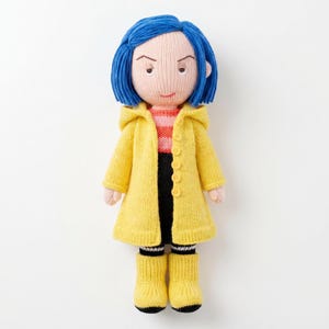 May include: A knitted doll with bright blue hair, wearing a yellow hooded raincoat with buttons, a pink and orange striped shirt, black trousers, and yellow boots with black trim. The doll has a pale complexion and a neutral facial expression.