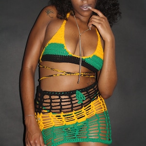 Puede incluir: Un conjunto de bikini de crochet con top y falda en los colores de la bandera de Jamaica. El top es de estilo halter y la falda es una minifalda con un patrón de crochet.