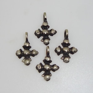 Könnte beinhalten: Vier silberne Kreuzanhänger mit einer strukturierten Oberfläche und fünf erhabenen Punkten auf jedem Kreuz.