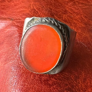 Puede incluir: Un anillo de plata con una piedra de cornalina naranja de forma ovalada engastada en una banda de plata trenzada.