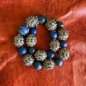 Puede incluir: Una taza de cerámica blanca con asa negra y el texto "But First, Coffee" en negrita negra. La taza se encuentra sobre un fondo borroso, sugiriendo un ambiente acogedor.