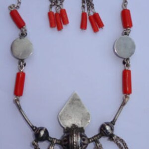 K&ouml;nnte beinhalten: Eine silberne Halskette mit roten Korallenperlen und einem silbernen Anh&auml;nger in Tropfenform. Die Halskette hat eine silberne Kette mit einem silbernen Verschluss. Der Anh&auml;nger hat ein silbernes Design in Tropfenform. Die Halskette wird mit einem Paar silberner Ohrringe mit roten Korallenperlen geliefert.