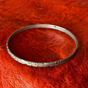 Può includere: Un braccialetto rigido in argento con un design inciso decorativo. Il braccialetto è sottile e ha uno stile semplice ed elegante.