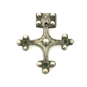 Puede incluir: Un colgante de cruz de plata con una parte superior cuadrada y un diseño circular. La cruz tiene una superficie texturizada y está decorada con pequeñas cuentas redondas.