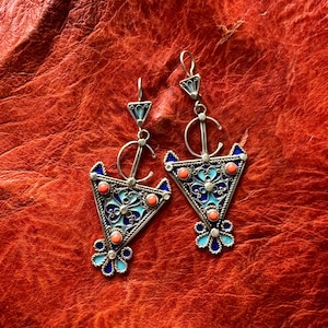 May include: A pair of silver earrings with a triangular design. The earrings are decorated with blue and white enamel and have coral-coloured stones.