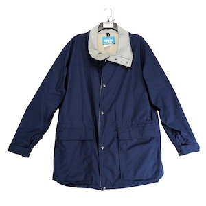 May include: A navy blue jacket with a light gray collar and a matching light gray lining. The jacket has two large front pockets, a drawstring waist, and a button-up closure. The jacket is hanging on a hanger.