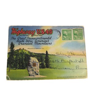 May include: Vintage postcard featuring a scenic view of the U.S. 40 highway, with text that reads "The Great Transcontinental Route thru America's Grandest Mountains." Includes two 1-cent postage stamps and handwritten address.