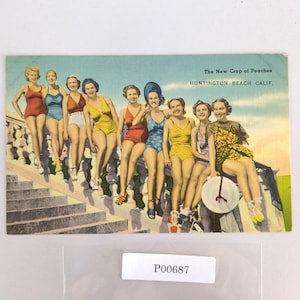 May include: Vintage postcard featuring a group of women in colorful swimsuits, posing on a stone structure. The text reads "The New Crop of Peaches, Huntington Beach Calif."
