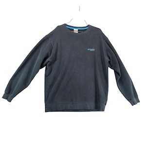 May include: A dark gray sweatshirt with long sleeves, a crew neck, and a blue trim. The Columbia logo is embroidered in light blue on the upper left chest. The sweatshirt is hanging from a metal hanger.