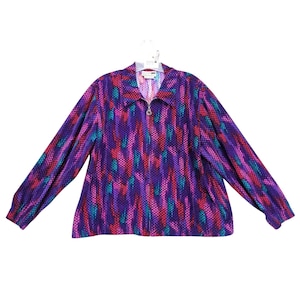 May include: A long-sleeved purple top with a textured pattern of vertical lines in teal, pink, and purple. The top has a collared neckline and a silver zipper. The garment is hanging on a white hanger.
