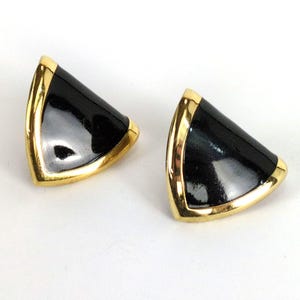 May include: A pair of black and gold earrings. Each earring is a triangle shape with a glossy black surface and a gold-colored border. The earrings are displayed on a white background.