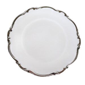 May include: A white ceramic plate with a scalloped edge and a silver-colored trim. The plate has a simple, elegant design, suitable for serving food. The plate is round and has a smooth surface.