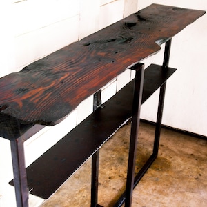 May include: A rustic wooden console table with a live edge top and a black metal frame. The table has two shelves.