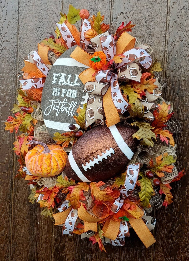 May include: A brown and orange fall wreath with a football theme. The wreath is decorated with fall leaves, pumpkins, and a football. The sign on the wreath says "Fall is for Football".