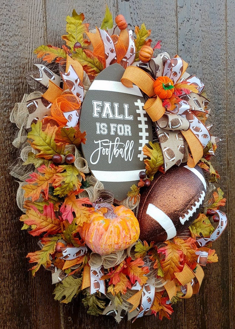 May include: A fall-themed wreath with a brown football, orange and brown ribbons, and fall leaves. The wreath has a sign that says "Fall is for Football".