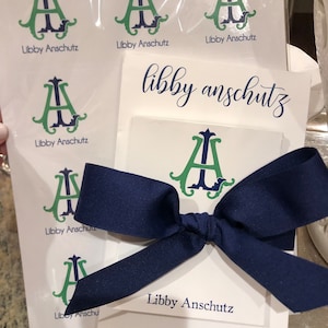 May include: A stationery set with a monogram design featuring the initials "A" and "I" in green and navy blue. The set includes notecards, stickers, and a navy blue ribbon. The text "Libby Anschutz" is printed on the items.