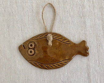 May include: A brown ceramic fish ornament with a string for hanging. The fish has two eyes and a textured surface.
