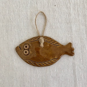 May include: A brown ceramic fish ornament with a string for hanging. The fish has two eyes and a textured surface.
