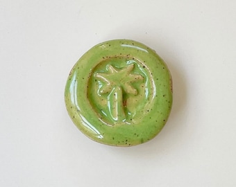 May include: A green ceramic tile with a raised design of a palm tree.
