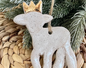 May include: A white ceramic reindeer ornament with a gold crown. The ornament has a speckled finish and is hanging from a twine string.