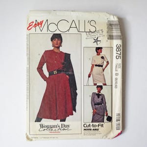 Peut inclure: Une pochette de patron de couture McCall's numéro 3875, taille B (8, 10, 12). Le devant présente des illustrations de trois modèles de robes, dont une robe rouge avec une ceinture et un châle noirs, une robe blanche et une robe grise.