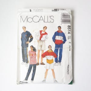 Peut inclure: Une enveloppe de patron en papier blanc avec le logo McCall's et des illustrations de vêtements de sport. L'enveloppe présente des images d'un survêtement bleu et rouge, d'une chemise rayée rouge et blanche et d'un short.
