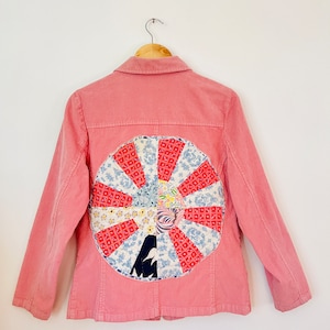 May include: A pink corduroy jacket with a large, colorful patchwork circle on the back. The circle is made of various fabrics in shades of red, blue, white, and green.