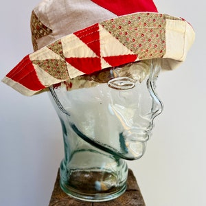 May include: A red, white, and brown patchwork bucket hat with a geometric pattern. The hat is on a glass mannequin head.